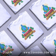 Футболка намасте бічес, біла, зображена з фронтального ракурсу на манекені, фон світло-сірий, принт з зображенням складених рук у позі намасте, кольорові деталі з зеленим фоном та написом 'NAMASTE BITCHES' у червоному та чорному кольорах.