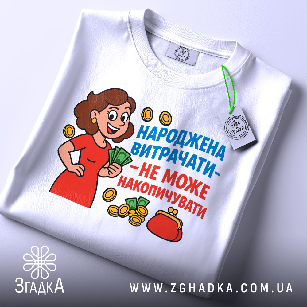 Футболка народжена витрачати, біла, зображена з верхнього ракурсу, фон світло-сірий, принт з жінкою в червоній сукні, яка тримає гроші, текст яскравий, синій та червоний, на комірці є етикетка з зеленим шнурком.