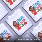 Футболка народжена витрачати, біла, зображена з фронтального ракурсу на манекені, фон світло-сірий, принт з веселою жінкою в червоній сукні, яка тримає гроші, оточена монетами та гаманцем, текст яскравий, синій та червоний.