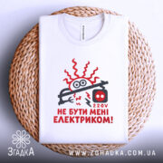 Футболка не бути електриком. Біла футболка, що лежить на плетеній основі, з принтом червоного кольору, зображення електричного шнура та написом "НЕ БУТИ МЕНІ ЕЛЕКТРИКОМ!". Фон світло-сірий, текстура плетеної основи добре видна.