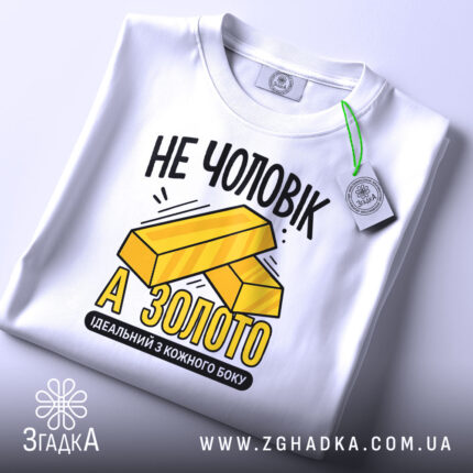 Футболка не чоловік а золото. Біла футболка, зображена зверху, з етикеткою на зеленому шнурку. Фон світло-сірий. Принт з жовтими злитками золота та текстом "НЕ ЧОЛОВІК А ЗОЛОТО" в чорному кольорі.