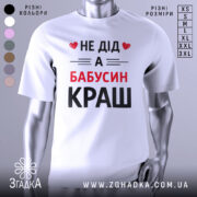Футболка не дід а бабусин краш. Біла футболка з коротким рукавом, зображена з фронтального ракурсу на манекені. На футболці великий принт чорного та червоного кольорів з текстом 'НЕ ДІД А БАБУСИН КРАШ'. Фон світло-сірий, що підкреслює яскравість принта.
