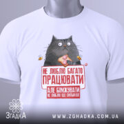 Футболка не люблю працювати, білого кольору, зображена зверху на столі, фон світло-сірий, принт з котом, що тримає шматок їжі, з текстом червоного кольору, на комірці є етикетка.