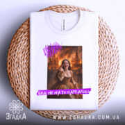 Футболка не на то нарвались. Біла футболка, складена на плетеній основі, з принтом дівчини в коричневій сукні на фоні з вогнем, текст на фіолетовому фоні.