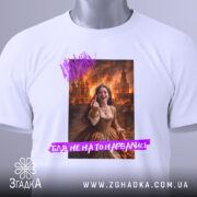 Футболка не на то нарвались. Біла футболка, складена на поверхні, з принтом дівчини в коричневій сукні, фон з вогнем. На футболці є етикетка з зеленим шнурком.