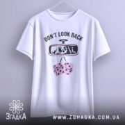 Футболка не озирайся назад. Біла футболка, підвішена на вішалці, з фронтального ракурсу. Принт на футболці містить напис 'DON'T LOOK BACK' та малюнок дзеркала заднього виду з черепом і кістками. Фон світло-сірий, що створює контраст з футболкою.