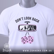 Футболка не озирайся назад. Біла футболка, складена на поверхні, з видимим принтом. На футболці напис 'DON'T LOOK BACK' та малюнок дзеркала заднього виду з черепом і кістками. Фон світло-сірий, а на футболці видно етикетку з зеленим шнурком.