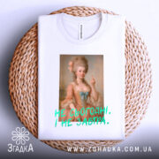 Футболка не сьогодні не завтра. Біла футболка, складена на плетеній кошику, з принтом жінки в історичному вбранні, що показує середній палець. Текст яскравий, зелений, розташований під зображенням.