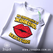 Футболка не сперечайся з жінкою. Білий колір, зображена в складеному вигляді, фон світло-сірий, принт з червоними губами та жовтим текстом, на ярлику зелена стрічка.