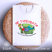 Футболка не турбувати, біла, з принтом на грудях, зображення хлопця на зеленому дивані, газета в руках, текст червоним кольором, складена на плетеній основі.