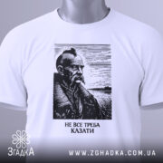 Футболка не все треба казати, біла, складена на поверхні, фон світлий, принт з портретом чоловіка з вусами та бородою, напис під портретом: 'НЕ ВСЕ ТРЕБА КАЗАТИ', на етикетці зелена стрічка.