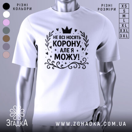 Футболка не всі носять корону. Біла футболка на манекені, з принтом чорного кольору, на якому написано 'НЕ ВСІ НОСЯТЬ КОРОНУ, АЛЕ Я МОЖУ!'. Фон світло-сірий, з легким градієнтом.