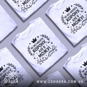 Футболка не всі носять корону. Біла футболка на манекені, з принтом чорного кольору, на якому написано 'НЕ ВСІ НОСЯТЬ КОРОНУ, АЛЕ Я МОЖУ!'. Фон світло-сірий, з легким градієнтом.