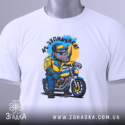 Футболка не зупиняйся. Біла футболка, складена на поверхні, з принтом носорога в жовтій куртці на мотоциклі, фон світло-сірий, на футболці є етикетка з зеленим шнурком.