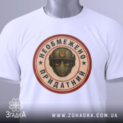 Футболка необмежено придатний, білого кольору, складена на поверхні, фон світло-сірий, принт у центрі з зображенням шолома та написом, прикріплена етикетка з зеленим шнурком.