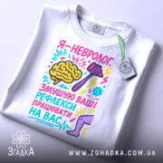 Футболка невролог білого кольору, складена на столі, фон світлий, принт яскравий, з малюнком мозку, молотка та ноги, текст кольоровий, з елементами графіки, на футболці є бірка.