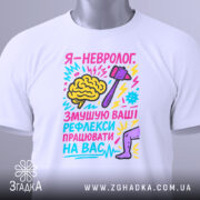 Футболка невролог білого кольору, складена на столі, фон світлий, принт яскравий, з малюнком мозку, молотка та ноги, текст кольоровий, з елементами графіки, на футболці є бірка.