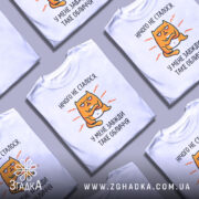 Футболка нічого не сталося. Біла футболка на манекені, з принтом жовто-оранжевого кота з виразом обличчя, що говорить 'У МЕНЕ ЗАВЖДИ ТАКЕ ОБЛИЧЧЯ'. Фон світло-сірий, футболка має короткі рукави і округлий виріз.