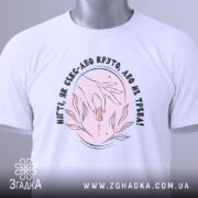 Футболка нігті як секс, складена футболка на білому фоні, зображення зверху, принт з руками та флакончиком, текст чорного кольору, етикетка з зеленим шнурком.