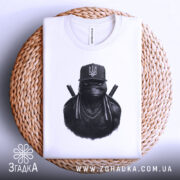 Футболка ніндзя український дух, біла, складена на кошику, фон світло-сірий, принт з ніндзя в чорному капелюсі з гербом України, видно етикетку з логотипом.