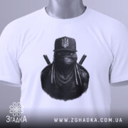 Футболка ніндзя український дух, біла, складена на столі, фон світло-сірий, принт з ніндзя в чорному капелюсі з гербом України, прикріплена етикетка з логотипом.