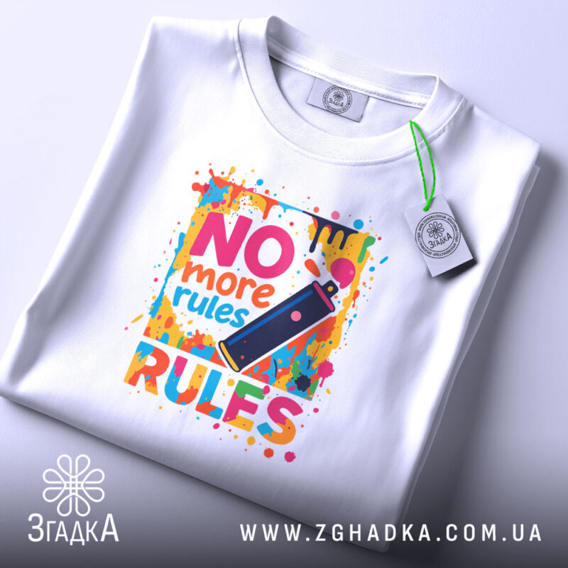 Футболка No more rules білого кольору, зображена зверху, на ній яскравий принт з написом 'NO more rules' та малюнком балончика з фарбою, фон світлий, на футболці є етикетка з зеленим шнурком.