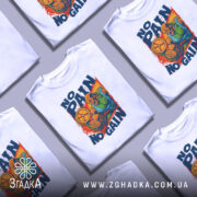 Футболка No Pain No Gain білого кольору, зображена на манекені з правого боку, фон світло-сірий, принт зображає м'язистого чоловіка, який піднімає обруч, з написом 'NO PAIN NO GAIN' у яскравих кольорах.