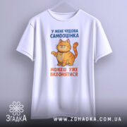 Футболка нормальна самооцінка. Біла футболка з принтом, на якому зображений усміхнений кіт оранжевого кольору. Принт розташований на грудях, текст синього та оранжевого кольорів. Фон світло-сірий, футболка представлена на манекені.