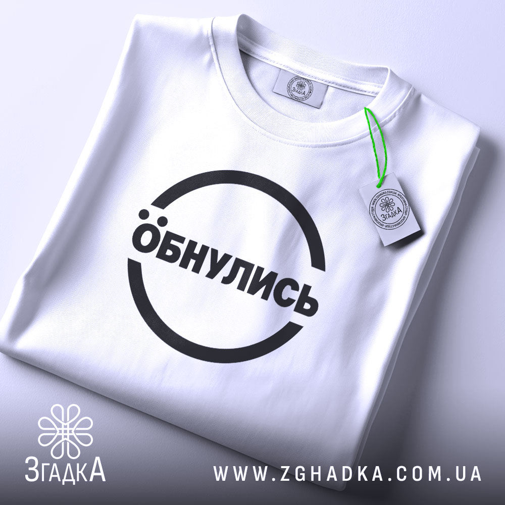 Футболка обнулись стильний мінімалізм, біла, складена на поверхні, фон світло-сірий, принт чорний з написом 'Обнулись' у колі, на комірці є етикетка.