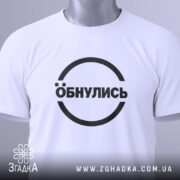 Футболка обнулись стильний мінімалізм, біла, складена на поверхні, фон світло-сірий, принт чорний з написом 'Обнулись' у колі, на комірці є етикетка.