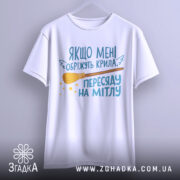 Футболка обріжуть крила, біла, підвішена на вішалці, зображена з фронтального ракурсу, фон світло-сірий, принт містить текст та малюнок мітли, виглядає стильно.
