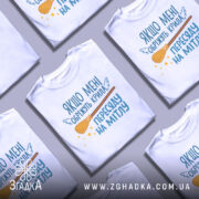 Футболка обріжуть крила, біла, зображена з фронтального ракурсу, на фоні світло-сірого градієнту, принт містить текст з жартівливим змістом та малюнок мітли з зірочками.