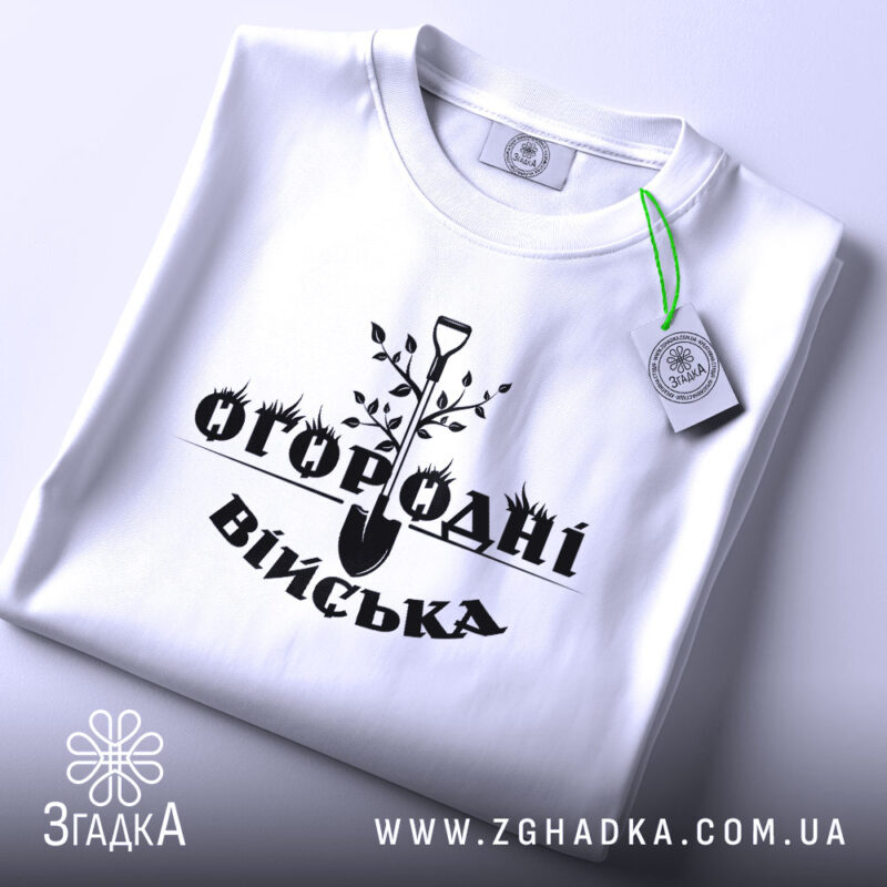 Футболка огородні війська, біла, складена на поверхні, з видимим етикеткою, фон світло-сірий, принт чорного кольору з лопатою та рослинами.