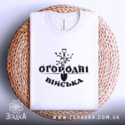 Футболка огородні війська, біла, складена на плетеній основі, фон світло-сірий, принт чорного кольору з лопатою та рослинами.