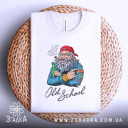 Футболка Old School білого кольору, складена на плетеній кошику, з принтом старшого чоловіка з бородою, який тримає пляшку та сигару, фон світло-блакитний, деталі принта чіткі.