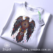 Футболка орел бойовий дух, біла, зображена зверху, складена на поверхні, фон світло-сірий, принт з орлом в червоних, чорних і золотих кольорах, з етикеткою на зеленому шнурку.