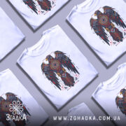 Футболка орел бойовий дух, біла, зображена з фронтального ракурсу на манекені, фон світло-сірий, принт з орлом в червоних, чорних і золотих кольорах, деталі геометричні та символічні.
