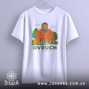 Футболка Овруч білого кольору, зображена з фронтального ракурсу на вішалці, фон світло-сірий, принт з зображенням церкви з червоної цегли та зеленими деревами, напис OVRUCH під малюнком.