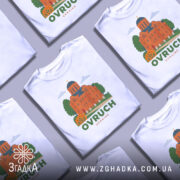 Футболка Овруч білого кольору, зображена з фронтального ракурсу на манекені, фон світло-сірий, принт з зображенням церкви з червоної цегли та зеленими деревами, напис OVRUCH під малюнком.