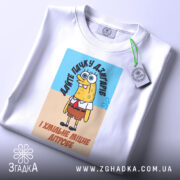 Футболка пачку дзигарів, біла, з ракурсом зверху, на фоні світло-сірого кольору, принт з персонажем у жовтому кольорі, з етикеткою зеленого кольору.