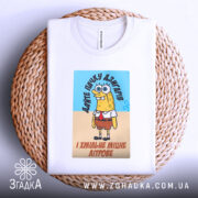 Футболка пачку дзигарів, біла, з ракурсом зверху, на фоні плетеного кошика, принт з персонажем у жовтому кольорі, з написом українською мовою.