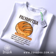 Футболка паляниця, білого кольору, зображена з верхнього ракурсу, фон світлий, на футболці є етикетка з зеленим шнурком, принт з малюнком хліба та текстом українською мовою.