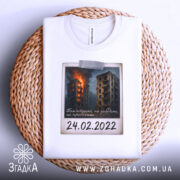 Футболка памʼять 24 лютого, біла, складена на плетеній основі, фон натуральний, принт з палаючими будинками, напис "24.02.2022" наклеєний.