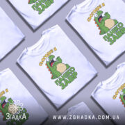 Футболка панікозавр білого кольору, зображена з фронтального ракурсу на манекені, фон світло-сірий, принт з веселим динозавром та написом 'Сьогодні я панікозавр' у зелених тонах.