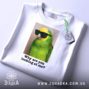 Футболка папуга у окулярах, біла, складена на поверхні, фон світло-сірий, принт з зеленим папугою в окулярах, текст під ним: 'Why are you looking at me?', на футболці є етикетка з зеленим шнурком.