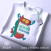 Футболка патякала позакривали, біла, зображена зверху, фон світлий, принт з монстром, який піднімає руки, кольори принта червоний, зелений, жовтий та блакитний, на футболці є етикетка.