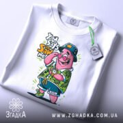 Футболка патрик у відпустці, біла, складена на поверхні, фон світлий, принт з мультяшним персонажем у зеленій сорочці з квітковим малюнком, з годинником на руці та капелюсі, прикріплена етикетка.