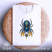 Футболка павук з тризубом, біла, зображена зверху, фон світло-сірий, принт з павуком синього кольору з жовтими деталями, футболка лежить на плетеній основі.