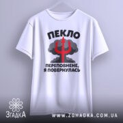 Футболка пекло переповнене, біла футболка на вішалці, з кольоровим принтом, що містить текст "ПЕКЛО ПЕРЕПОВНЕНЕ, Я ПОВЕРНУЛАСЬ" та червоний тризуб на фоні хмар.