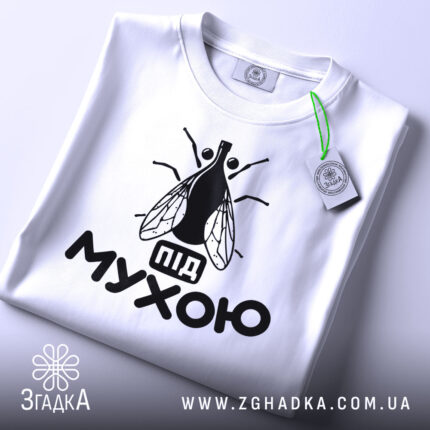 Футболка під мухою білого кольору, зображена зверху, на ній видно чорний принт з малюнком мухи та написом 'під мухою', на комірці є етикетка.